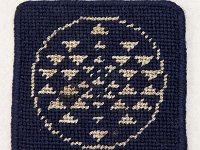 BSG insignia coaster: Canvas needlework coaster showing the Battlestar Galactica insignia. Artist is unknown. (MsC 0960)
